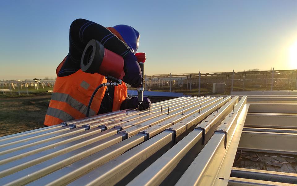 Installer holding drill over metal bars with solar panel installation in background